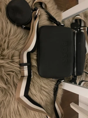 Äkta axelväska ifrån BOSS - Säljer min axelväska från boss som jag knappt använt och köptes förra året, modellnumret är 50523408 och den är helt äkta och köptes på thernlunds. Fler bilder kan skickas. 
