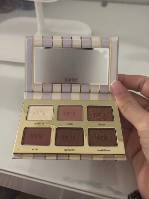 Tarte ögonskuggspalett med spegel - Snygg ögonskuggspalett från Tarte med sex nyanser: skimrande champagne, matt rosa, glittrig brun, matt vinröd, matt brun och mörkbrun med skimmer. Paletten har en lyxig design med guldiga detaljer och inbyggd spegel. Perfekt för att skapa olika ögonlooks.