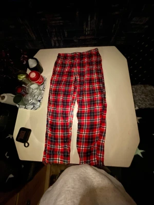 Rödrutiga pyjamasbyxor - Mysiga pyjamasbyxor i klassiskt röd- och svart-rutigt mönster. Tillverkade i mjuk bomull med resår i midjan för extra komfort. Perfekta för chillkvällar hemma eller när du vill ha det extra bekvämt.