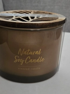 Doftljus i glas med trälock - Säljer ett naturligt doftljus av sojavax i glasburk med dekorativt trälock med utskuret bladmotiv. Ljusets färg är beige och texten på burken är i guld. Perfekt för att skapa mysig stämning hemma.