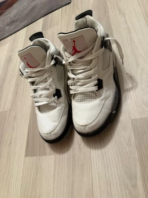 Vita Air Jordan 4 Retro sneakers - Säljer ett par vita Air Jordan 4 Retro sneakers med svarta och grå detaljer. Skorna har meshpaneler på sidorna, synlig Air sula och klassisk high top siluett. 