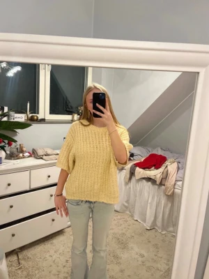 Gul stickad tröja med kort ärm - Säljer en söt, ljusgul stickad tröja med korta ärmar och rund hals. Tröjan har en oversized passform och är stickad i ett grovt garn som ger en mysig känsla. Perfekt att styla med jeans för en avslappnad look.