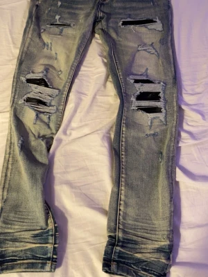 Amiri jeans - Säljer ett par ljusblå jeans med kraftigt slitna detaljer och stora hål på framsidan. Jeansen har en rak passform och tydliga slitningar vid benslut och bak. Perfekt för dig som gillar en edgy och trendig look.