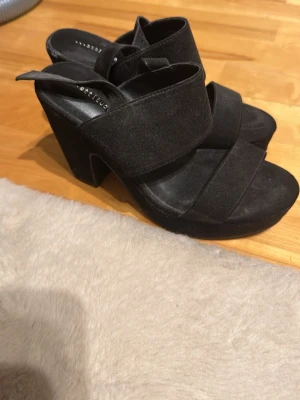 Svarta chunky sandaler - Säljer ett par svarta sandaler med breda band över foten och öppen tå. Skorna har chunky klack och platåsula för extra höjd och stabilitet. Materialet är mockaimitation som ger en snygg och trendig look.