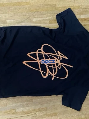 Svart t-shirt med orange print - Cool svart t-shirt från OOCI med ett stort orange abstrakt print på framsidan och blå textdetalj. Perfekt för dig som gillar unika och grafiska motiv. Klassisk passform och korta ärmar, tillverkad i mjuk bomull.