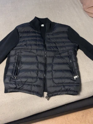 Moncler cardigan - Säljer en svart cardigan från Moncler med quiltad front och två dragkedjeförsedda fickor. klassisk Moncler-logga på ärmen. Perfekt för lager-på-lager och snygg att matcha med hoodie eller t-shirt.