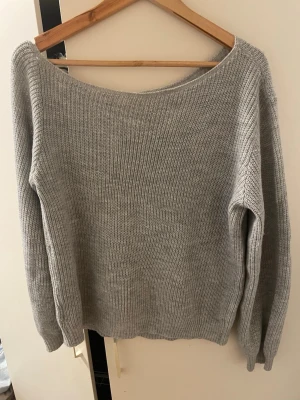 Ljusgrå oversized stickad tröja - Mysig ljusgrå stickad tröja med bred halsringning och långa ärmar. Tröjan har en avslappnad, oversized passform och ribbstickade muddar vid ärmslut och nederkant. Perfekt för lager på lager och chill dagar.