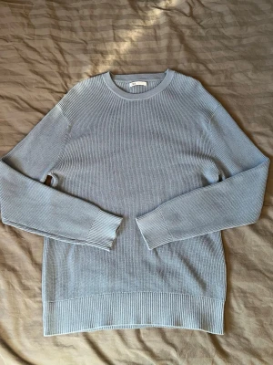 Blå stickad tröja från Zara - Här är en beskrivning av tröjan: Märke: ZARA Storlek: M Skick: Ny och oanvänd. Färg: Ljusblå (stålgrå nyans) Material: 100% bomull Beskrivning: Stilren och bekväm stickad tröja i en fin ljusblå färg med en subtil stålgrå nyans. Tröjan är rundhalsad och gjord i ribbstickad bomull, vilket ger en stretchig och skön passform. Den är perfekt för vardagsbruk och passar bra att matcha med jeans eller chinos. Modellen på bilden är 183 cm lång och väger 72 kg och bär storlek M, vilket ger en bra referens
