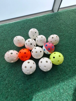 Samling innebandybollar i olika färger - Säljer en samling innebandybollar i plast, flera vita samt en orange, en gul och en vit/röd. Bollarna har klassiska hål och är runda. Perfekt för träning eller spel med kompisar.