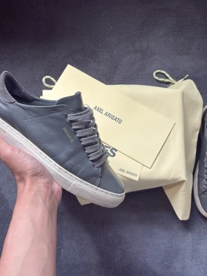 Axel arigato skor - Stilrena sneakers från Axel Arigato i exklusivt mörkgrått läder. Minimalistisk design med diskret logga på sidan som ger en lyxig och modern känsla.  Tillverkade med fokus på kvalitet och komfort – perfekta både till vardag och mer uppklädda outfits. Levereras med original dustbag och tillbehör.  Ett måste för dig som uppskattar clean, skandinavisk design med premiumkänsla.  Storlek: 40 passar 41 Skick: använt skick