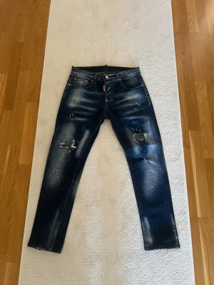 Dsquared2 jeans - Säljer ett par mörkblå jeans från Dsquared2 med slitningar och färgstänk. Jeansen är i fint skick och är använda mellan 5-10 gånger ungefär. Vid fler bilder eller frågor är det bara att höra av sig. Pris kan diskuteras!