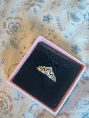 Pandora silver tiararing med pärldetaljer - Säljer en snygg silverring från Pandora i form av  en tiara. Ringen har små pärldetaljer längs kanten och ett elegant, kronliknande mönster. Perfekt för dig som gillar unika och stilrena smycken med en touch av prinsesskänsla.