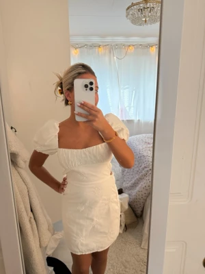 Zara klänning/studentklänning med puffärmar - Söt vit kort klänning med puffärmar och broderade blommor. Klänningen har en fyrkantig urringning och markerad midja som ger en feminin siluett. Perfekt för sommarens alla tillfällen och lätt att styla med accessoarer.