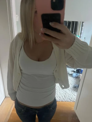 Vit kort kofta med ribbade muddar - Säljer en vit, kort kofta med långa ärmar och ribbade muddar. Koftan har en öppen front och är perfekt att slänga över ett linne eller t-shirt. Enkel och stilren design som passar till mycket.