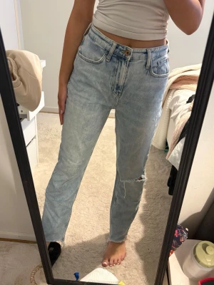 Ljusblå raka jeans med slitning - Säljer ett par ljusblå jeans med rak passform och hög midja. Jeansen har klassiska fem fickor och en cool slitning på ena knät. Perfekt för dig som gillar en avslappnad och trendig look.