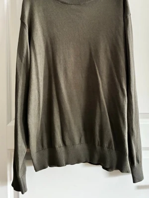 Olivgrön stickad tröja - En enkel och stilren olivgrön stickad tröja med rund halsringning och långa ärmar. Tröjan har ribbade muddar vid ärmslut och nederkant. Perfekt att matcha med jeans eller kjol för en avslappnad look. Lager 157