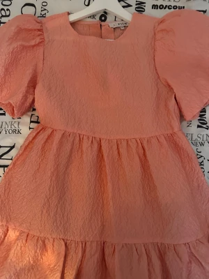 Rosa kort klänning från A View - Säljer en rosa kort klänning från A View med puffiga korta ärmar och strukturerat tyg. Klänningen har rund halsringning och volangdetaljer i kjolen. Perfekt för dig som gillar en feminin och trendig look.