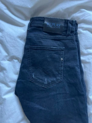 Mörkblå Replay jeans slim fit - Snygga mörkblå jeans från Replay med slim fit och klassiska bakfickor. Jeansen har diskreta slitningar och är tillverkade i mjukt denim-material. Perfekt för dig som gillar en stilren och modern look.
