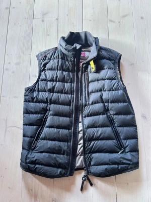 Svart dunväst från Parajumpers - Snygg svart dunväst från Parajumpers med quiltad design och gul detalj vid kragen. Västen har två dragkedjefickor fram och en hög krage. Tillverkad i superlätt material som håller värmen utan att kännas tung. Perfekt för lager på lager och streetstyle.