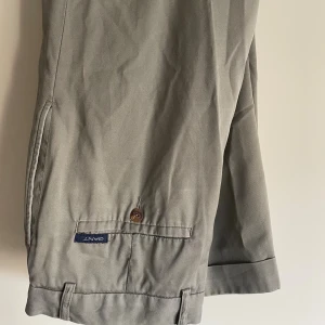 Gant chinos beige, storlek 28 - Klassiska beiga chinos från Gant med raka ben och snygga detaljer som bakficka med knapp och uppvikta benslut. Tillverkade i bomull för en skön och stilren känsla. Perfekta för en clean och avslappnad look. Lite äldre modell men elegant.