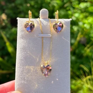 Smyckesset, brisyrkrok och halsband hjärtformade kristaller - Smyckesset, brisyrkrok och hänge i guldpläterad mässing med hjärtformade kristaller. Heart 11x10mm, färg Light Amethyst. Jag skickar endast spårbart, samfraktar. Fast pris. Besök gärna mina övriga annonser.  Till mina smycken använder jag kristaller från Preciosa, Aurora och Swarowski.