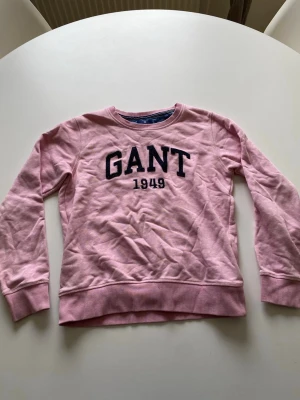 Rosa sweatshirt från GANT - Säljer en rosa sweatshirt från GANT med broderad logga och årtal 1949 på bröstet. Tröjan har rund halsringning, ribbade muddar och är tillverkad i mjukt bomullsmaterial. Perfekt för dig som gillar klassisk och avslappnad stil.
