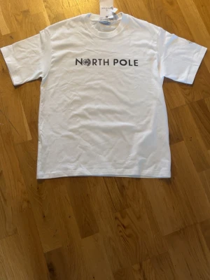 Vit North Pole t-shirt från Moncler - Vit t-shirt från Moncler med trycket 'North Pole' på bröstet. Klassisk rund hals och korta ärmar. Materialet är mjuk bomull och passformen är normal. Perfekt för dig som gillar stilrena och exklusiva plagg.