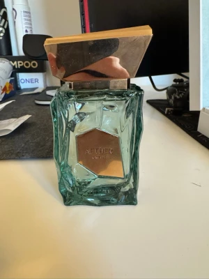 Aether från French Avenue - Unik parfymflaska i gröntonat glas med geometrisk, guldig metallkork och matchande gulddekor på framsidan. Doften heter Aether. Flaskan har en modern, edgy design som sticker ut på hyllan.