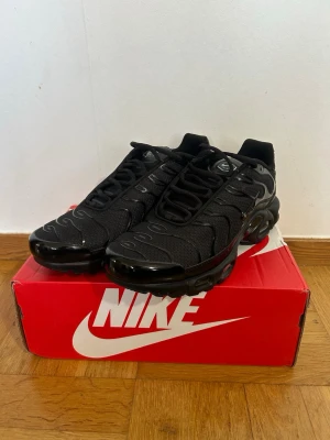 Nike Tn svart - Nike Air Max Plus sneakers i helsvart färg med mesh-överdel och syntetiska detaljer. Skorna har en chunky sula med Tuned Air-dämpning och ikoniska vågformade linjer på ovansidan. Perfekt för dig som gillar en sportig och modern look.