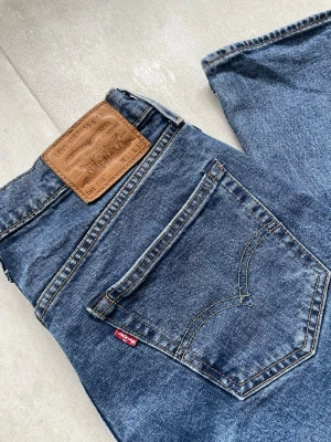 Levi's blå raka jeans 514 slim - Säljer ett par klassiska blå jeans från Levi's med raka ben och femficksdesign. Jeansen har en snygg läderpatch bak och ikonisk röd Levi's-tag på bakfickan. Materialet är slitstark denim i bomull och passformen är tidlös och enkel.