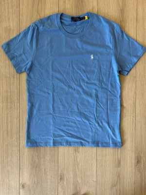 🩵Blå  Polo Ralph Lauren tshirt 🩵 - 🩵Snygg blå t-shirt från Polo Ralph Lauren med klassisk rund hals och korta ärmar. T-shirten har den ikoniska vita broderade loggan på bröstet och är gjord i mjuk bomull. Perfekt basplagg för en clean och stilren look. Passar dig som är 155-165 cm i längd. Tar emot bud, aldrig använd. Klassa storleken som xs inte M!!!!