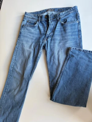 Blå regular fit jeans från Dressmann - Snygga blå jeans från Dressmann i regular fit-modell. Klassisk femficksdesign med dragkedjegylf och knapp. Jeansen är tillverkade i ett mjukt denimtyg som ger en avslappnad look. Perfekta för dig som gillar en tidlös och enkel stil.