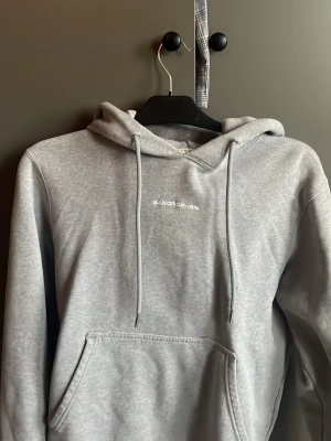 Grå hoodie från Sandro Paris - Snygg grå hoodie från Sandro Paris i utmärkt skick med broderad logga på bröstet.  Den har en justerbar huva med dragsko. Tillverkad i mjukt material som känns skönt mot huden. Perfekt för en avslappnad och trendig look.                         Hör gärna av dig vid frågor eller funderingar MVH Melker