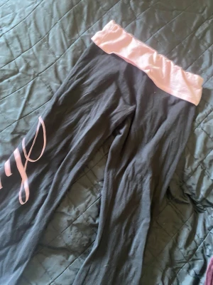 Svarta leggings med rosa detaljer - Coola svarta leggings med bred rosa linning och rosa text längs benet. Perfekta för chill eller träning, med mjukt och stretchigt material som sitter skönt. Snygg kontrast mellan svart och rosa, passar dig som gillar sportig stil.