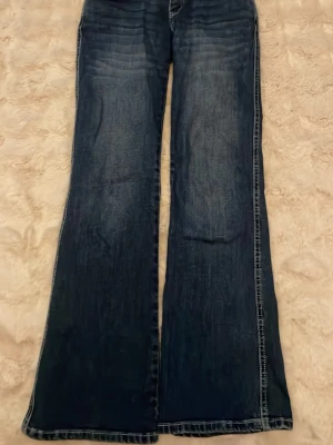 Mörkblå bootcut jeans - Säljer ett par mörkblå bootcut jeans med klassisk femficksdesign och lätt slitning på framsidan. Jeansen har breda ben och är tillverkade i denim. Perfekt för dig som gillar retrostil och vill ha ett par jeans med cool passform. Storlek S , pris 40 kr