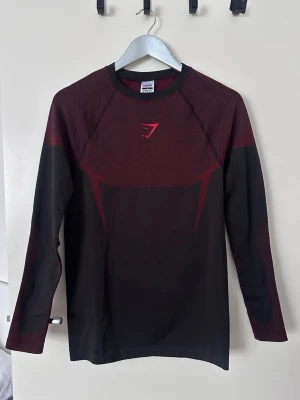 Svart och vinröd långärmad tröja Gymshark - Långärmad träningströja från Gymshark i svart och vinrött. Tillverkad i ett stretchigt och ventilerande material som passar perfekt för gym och träning. Aldrig använt den! Priset kan diskuteras