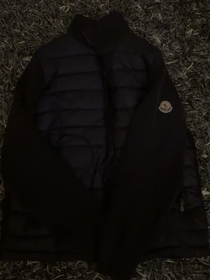 Mörkblå dunjacka från Moncler - Snygg mörkblå dunjacka från Moncler med klassisk quiltad design och hög krage. Jackan har dragkedja, Moncler-logga på ärmen och innerfoder med serietidningsmotiv. Perfekt för våren och även sommaren. Säljer jackan så billigt för taggen vid nacken har gott sönder. Pris kan diskuteras vid snabbaffär!