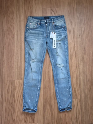 Sky blå slim fit distressed jeans från Purple - Snygga blå jeans från Purple med slitna detaljer och färgstänk. Modellen är slim fit med klassiska fem fickor och dragkedja. Perfekt för dig som gillar en trendig och avslappnad look.