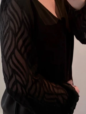 Svart härlig blus med chiffongärmar 🙌🏻! - En svart blus med chiffongärmar med resår i slutet, de är mönstrade och har en viss genomskinlighet. Regular passform. V-ringad. Klippt bort lapparna men det är strl M (se måtten nedan)  Tunt och skönt material nu inför våren och sommaren. Använd en gång bara. Polyester och chiffong. 