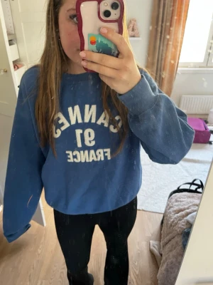 Blå sweatshirt från H&M med tryck - Blå sweatshirt från H&M med vitt tryck 'Cannes 91 France' på framsidan. Super snygg men kommer inte till någon användning⭐️