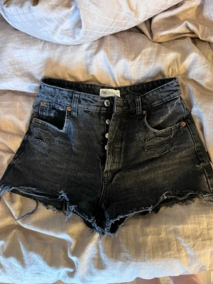 Svarta högmidjade jeansshorts från Zara - Säljer ett par svarta högmidjade jeansshorts från Zara med slitna detaljer. Fint skick💕