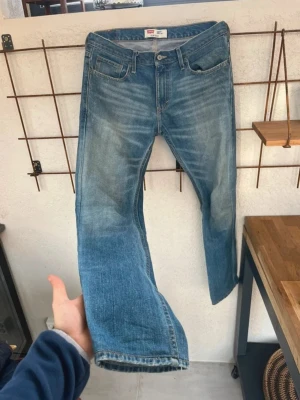 Levi's blå Bootcut jeans - Klassiska blå Bootcut ajeans från Levi's med fem fickor. Jeansen har en snygg tvättad look med slitningar och är tillverkade i denim. Perfekta för en avslappnad och trendig stil. Storlek W33 L34