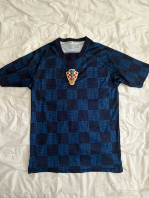 Blå-rutig fotbollströja Kroatien - Snygg blå fotbollströja med rutigt mönster i mörkblått och ljusblått. Tröjan har Kroatiens landslagsemblem på bröstet och är tillverkad i ett lätt och snabbtorkande material. Perfekt för träning eller match. Pris kan diskuteras 