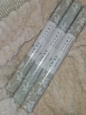 Grå tapetrullar med blommönster - Tre rullar tapet från Lycke i en mjuk grå nyans med vitt blommönster. Tapeterna är non-woven och har måtten 10,05 m x 0,53 m per rulle. Perfekt för att ge rummet en fräsch och stilren känsla med ett diskret mönster. 