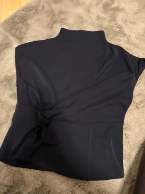 Mörkblå topp med knut - Snygg mörkblå topp med hög hals och  knut fram till. Med en tunndragkedja på ryggen