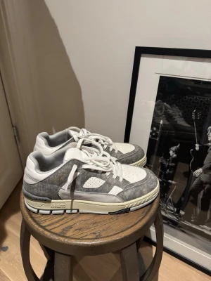 Gråvita sneakers från Axel Arigato - Snygga sneakers från Axel Arigato i grått och vitt. Skorna har en låg silhuett, perforerad tåbox och detaljer i mocka och läder. Klassisk snörning och robust sula för en trendig look. Perfekta för dig som gillar stilrena och moderna sneakers.