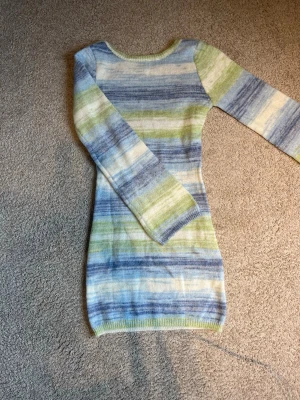 Randig stickad klänning i blått och grönt - Mysig stickad klänning med lång ärm och ur ringar rygg. Klänningen har ett randigt mönster i blå, grön, vit. Modellen är kroppsnära och kort. Aldrig använd!