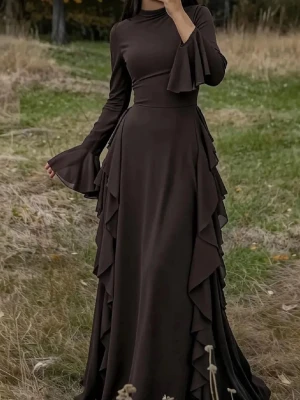 Mörkbrun långklänning med volang - Elegant mörkbrun långklänning med långa trumpetärmar och volangdetaljer längs sidorna. Klänningen har en hög hals och markerad midja som ger en snygg siluett. Perfekt för dig som vill sticka ut med en unik och stilren look.