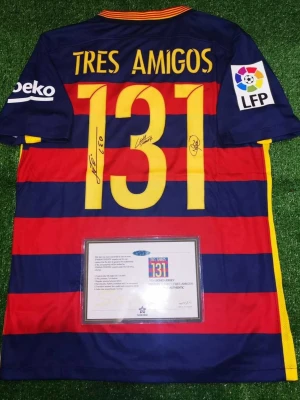 Barcelona Tres Amigos signerad matchtröja - Unik Barcelona matchtröja med blå och röda ränder, gula detaljer och texten 'TRES AMIGOS' samt siffran 131 på ryggen. Tröjan är signerad av tre spelare och har officiella klubbmärken och sponsorer på ärmarna. Perfekt för samlare eller fans.