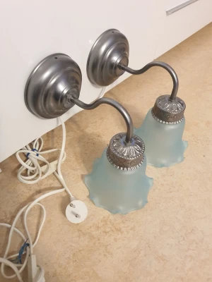 Vägglampor med glas - Säljer två snygga vägglampor i metall och dekorativa detaljer. Lamporna har rundad form och vågiga kanter på glaskuporna. Perfekt för dig som vill ha en unik belysning med vintagekänsla.